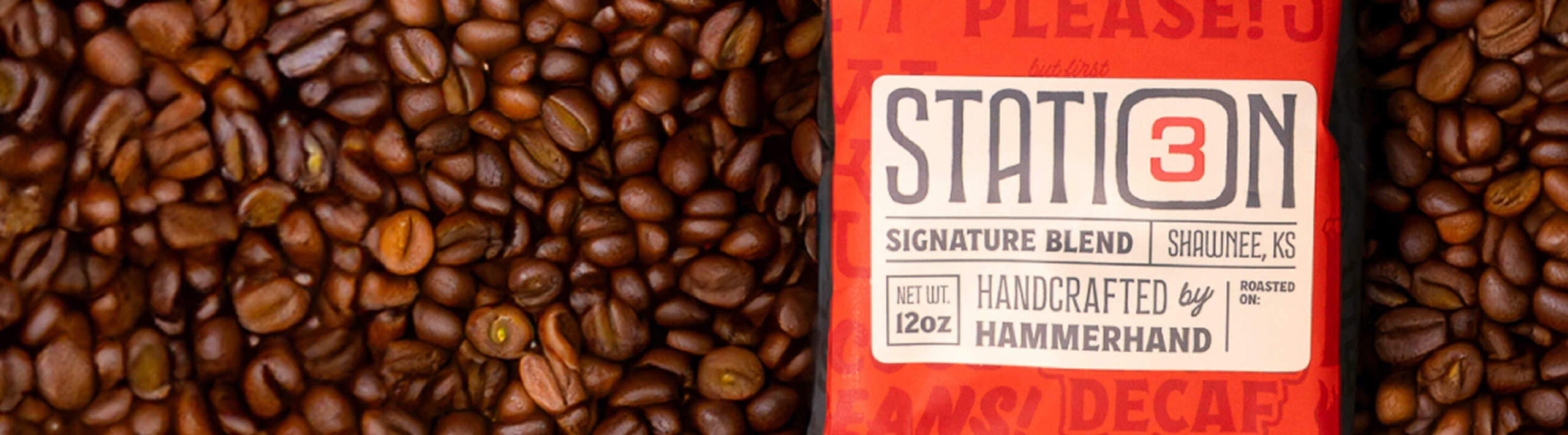 Close-up of Station 3 Signature Blend coffee bag surrounded by roasted coffee beans, labeled handcrafted by Hammerhand, 12oz.