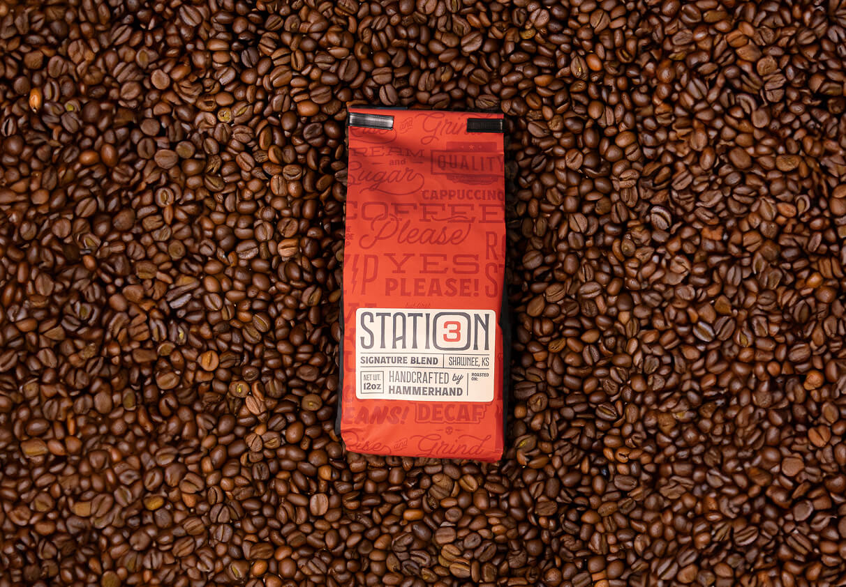 Red Station 3 Signature Blend coffee bag labeled handcrafted by Hammerhand, placed on a background of roasted coffee beans.